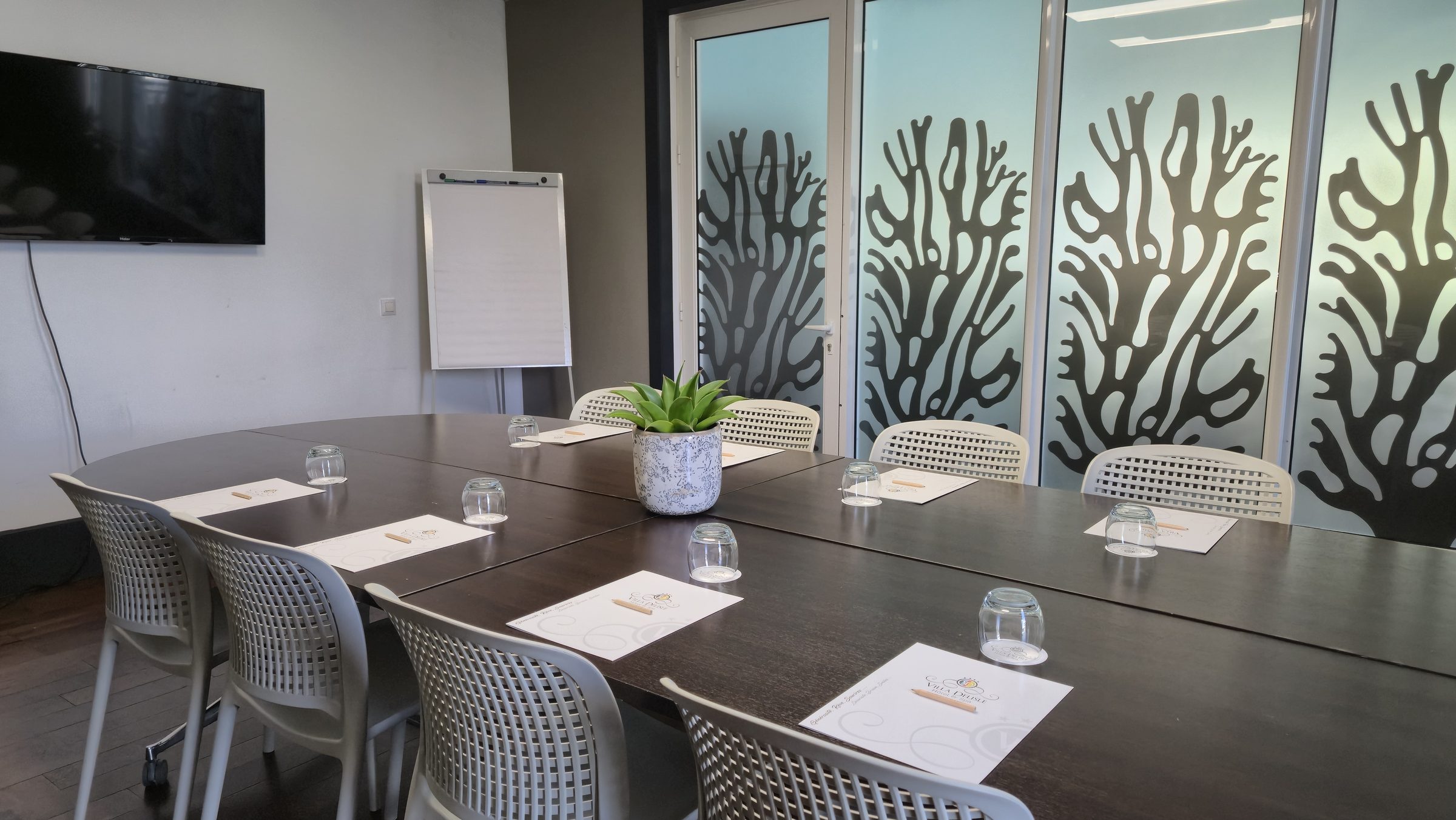 Salle de réunion dressée pour un séminaire : grande table, blocs-notes siglés, écran plat et paperboard